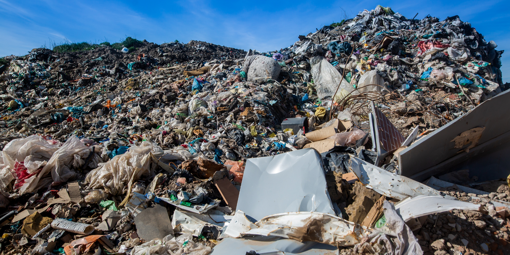 A sprawling landfill site with heaps of assorted waste and debris under a clear blue sky.
