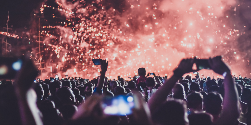 Crowd Of Music Festival Attendees With Phones Up Enjoying Pyrotechnic Display