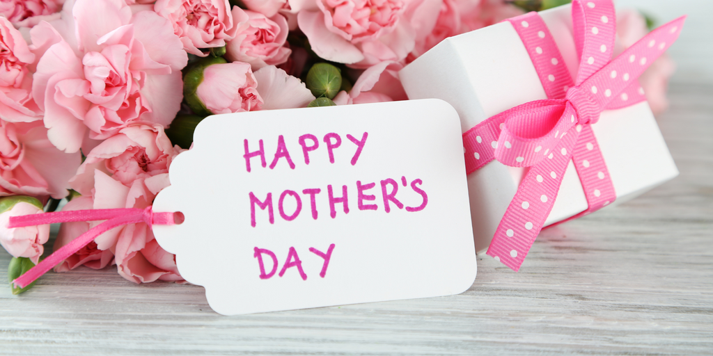 A bouquet of pink roses along with a gift box tied with a pink polka dot bow and a card saying "Happy Mother's Day"