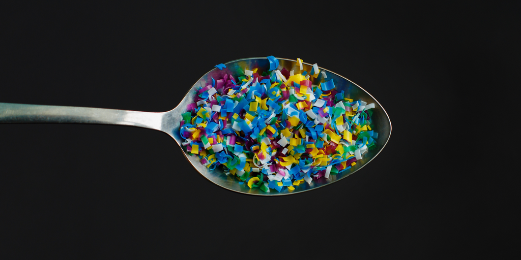 Understanding Microplastics - A Kitchen Spoon of Colorful Plastic Pieces Amidst a Black Background | EcoBlvd