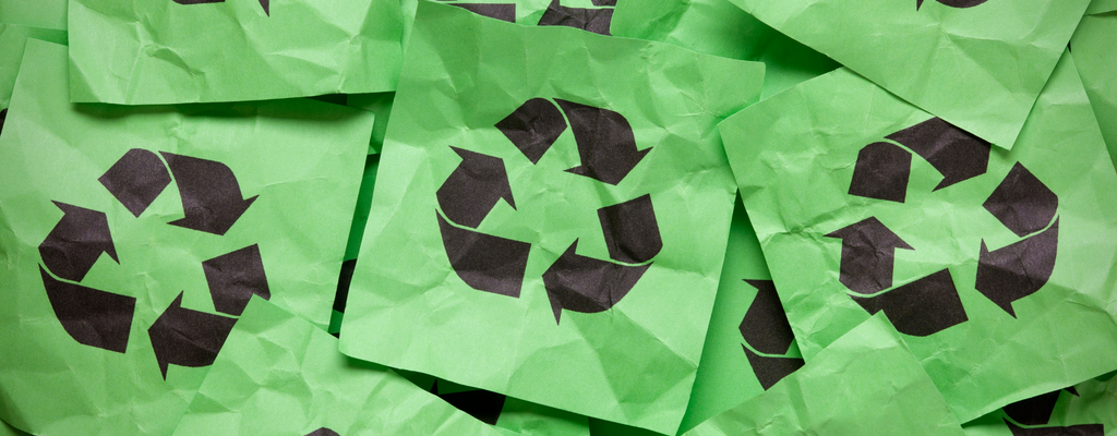 A pile of green papers with the recycling logo printed on them in black 