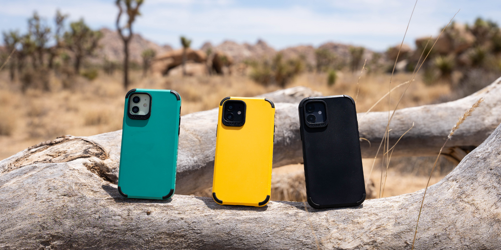 Rugged & Compostable Mojave Collection Phone Cases in Blue, Yellow, and Black Resting on a Wooden Log in a Serene Desert Landscape