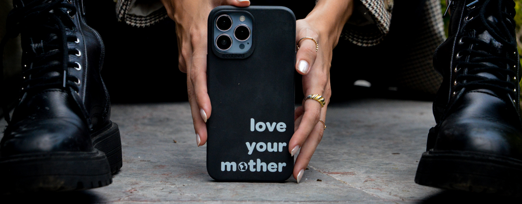 EcoBlvd - Woman Wearing Black Boots Holding Black Sequoia Collection Phone Case With The Love Your Mother Design For iPhone 